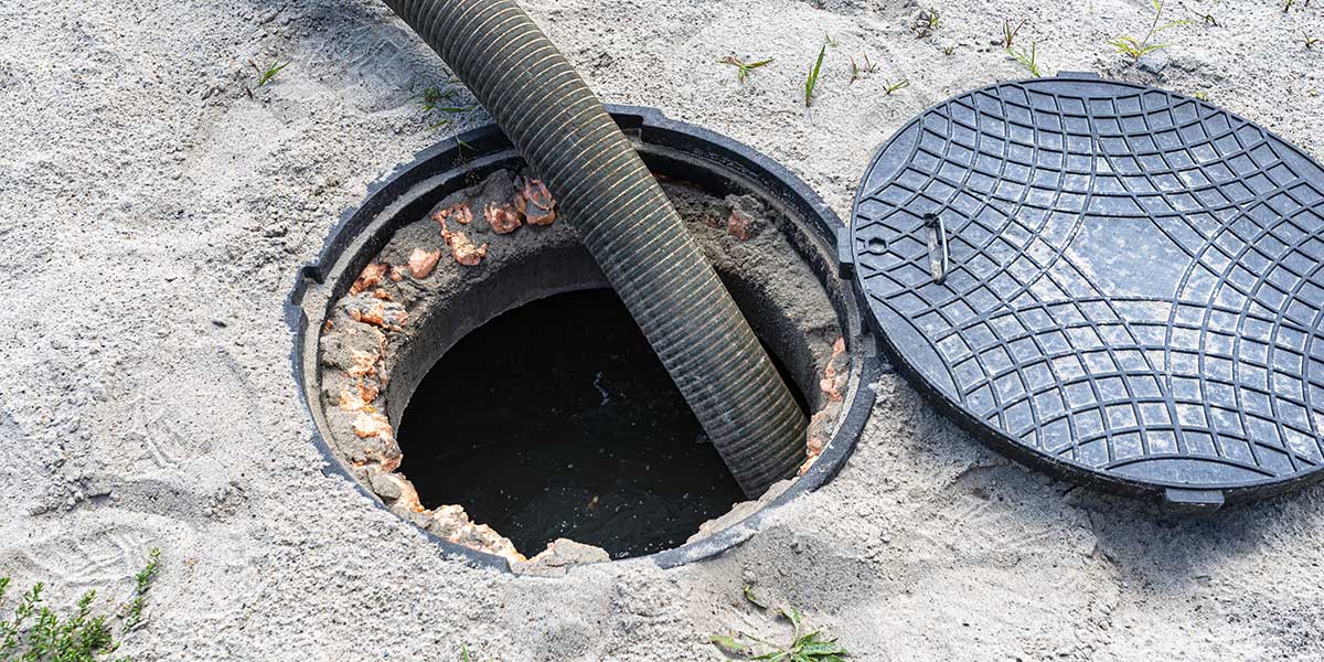 Open manhole with a large corrugated hose entering the shaft during sewer maintenance, sand around the rim and a closed manhole cover beside it