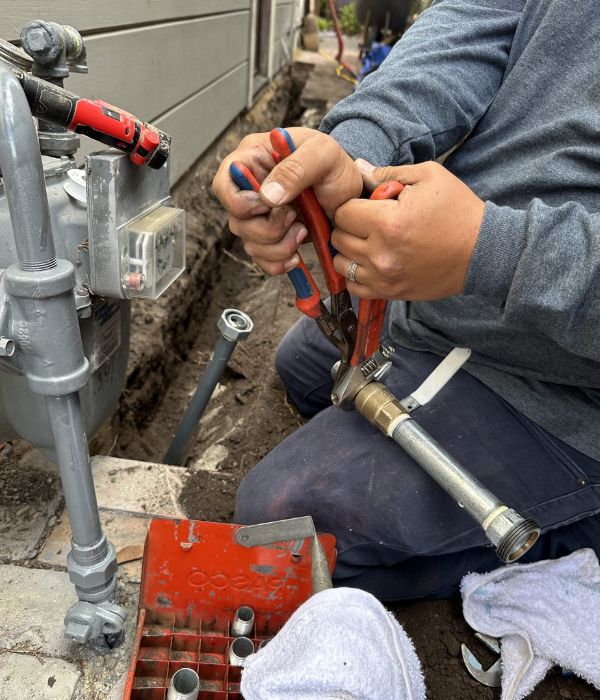A professional plumber performing gas line repair and installation services by tightening a brass fitting onto a utility pipe outside a home.