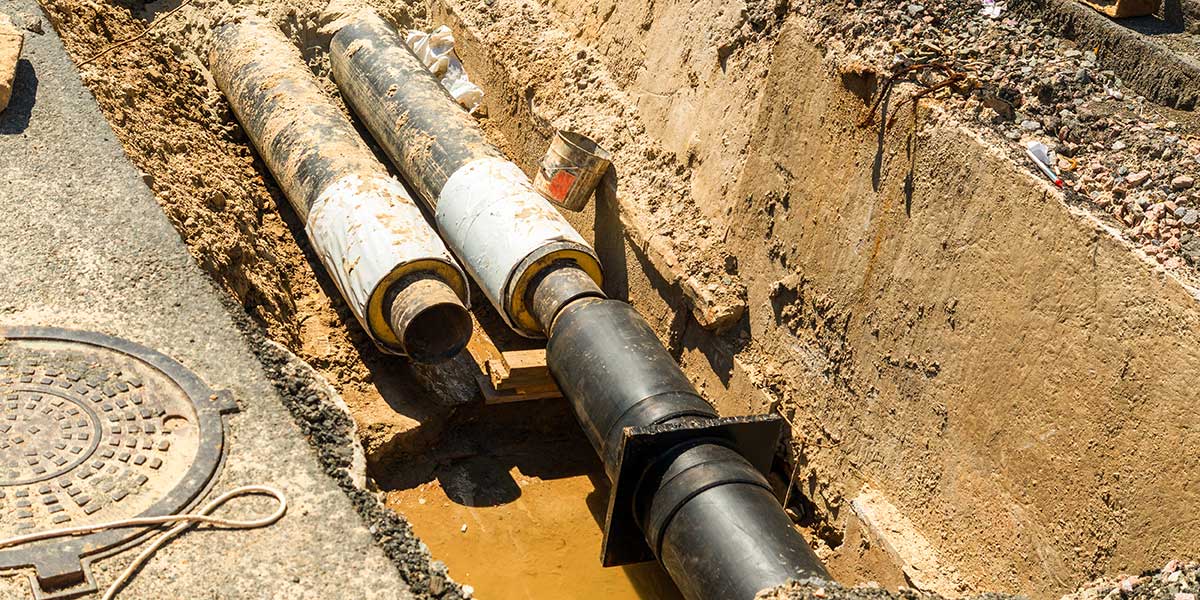 Exposed underground pipes lying in a deep dirt trench during an active residential sewer line repair and excavation project.